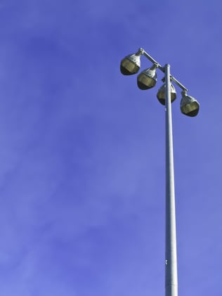 Row of four stadium lights atop metal pole on a sunny afternoon